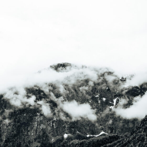 Schwarz/Weiß-Foto eine Bergspitze, welche im Nebel eingeschlossen ist